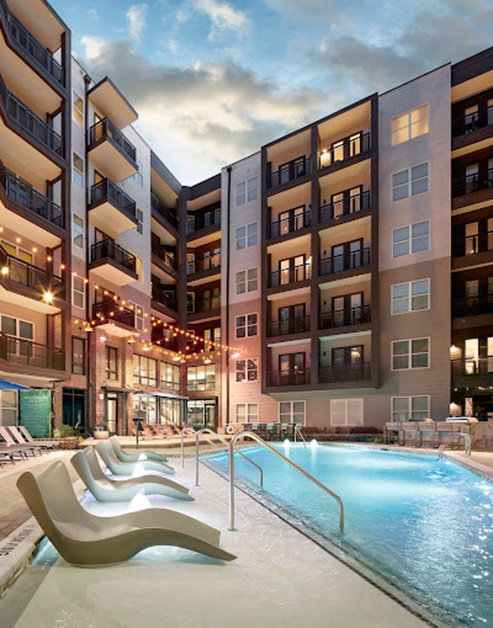 Resort-style pool at sunset with sundeck loungers, poolside lounge chairs situated under market lights in the center of the apartment complex at MAA LoSo luxury apartments in Charlotte, NC