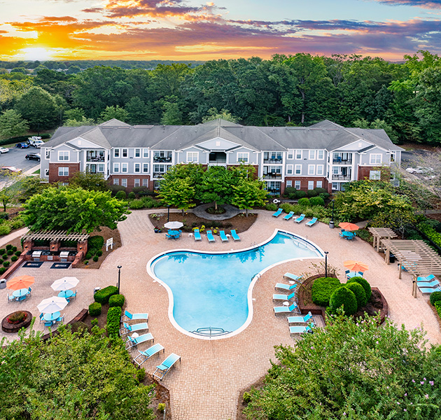 Community resort-style pool with lounge chairs and lush greenery situated next to the apartment building at MAA Matthews Commons luxury apartments in Matthews, NC