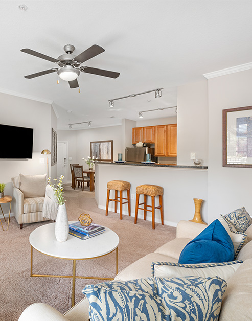 Living room area with wall mount TV next to kitchen bar top counter with bar stools at MAA Matthews Commons luxury apartments in Matthews, NC
