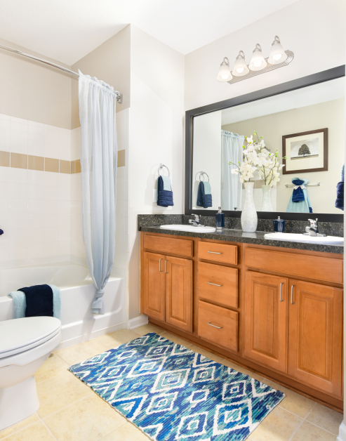 Bathroom with sleek light fixtures above dark granite countertop with double vanity sinks and light brown cabinets at MAA Matthews Commons luxury apartments in Matthews, NC