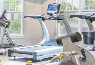 Close up of fitness center treadmill next to other workout machines next to large windows at MAA Matthews Commons luxury apartments in Matthews, NC