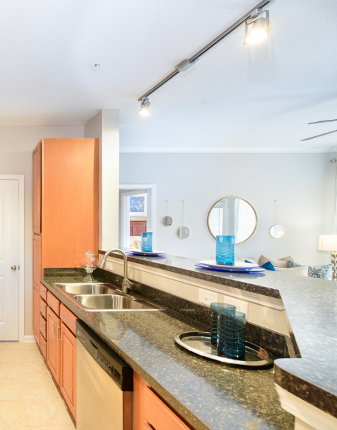 Modern-style kitchen with track lights above kitchen sink with granite bar top counter with light brown cabinets at MAA Matthews Commons luxury apartments in Matthews, NC