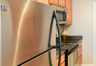 Close view of stainless-steel refrigerator and kitchen stove with light brown cabinets at MAA Matthews Commons luxury apartments in Matthews, NC