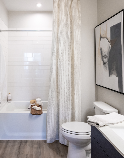 A modern bathroom with white countertops and dark cabinets, bathtub, and wood floors with wall art at MAA Optimist Park luxury apartments in Charlotte, NC