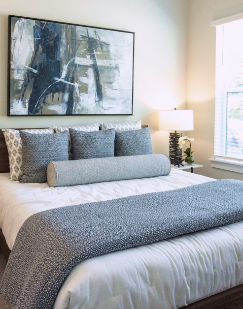 A luxurious model bedroom with blue décor, a stylish nightstand and a painting on the wall at MAA Optimist Park luxury apartments in Charlotte, NC