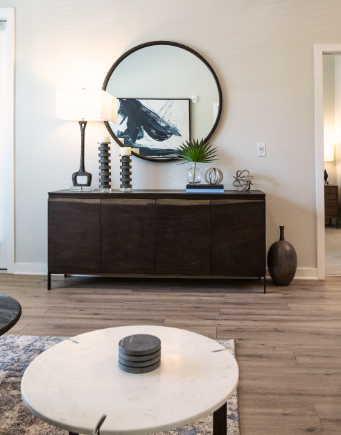 A stylish living room featuring a stylish white round coffee table and decorative circular wall mirror above wooden dresser at MAA Optimist Park luxury apartments in Charlotte, NC