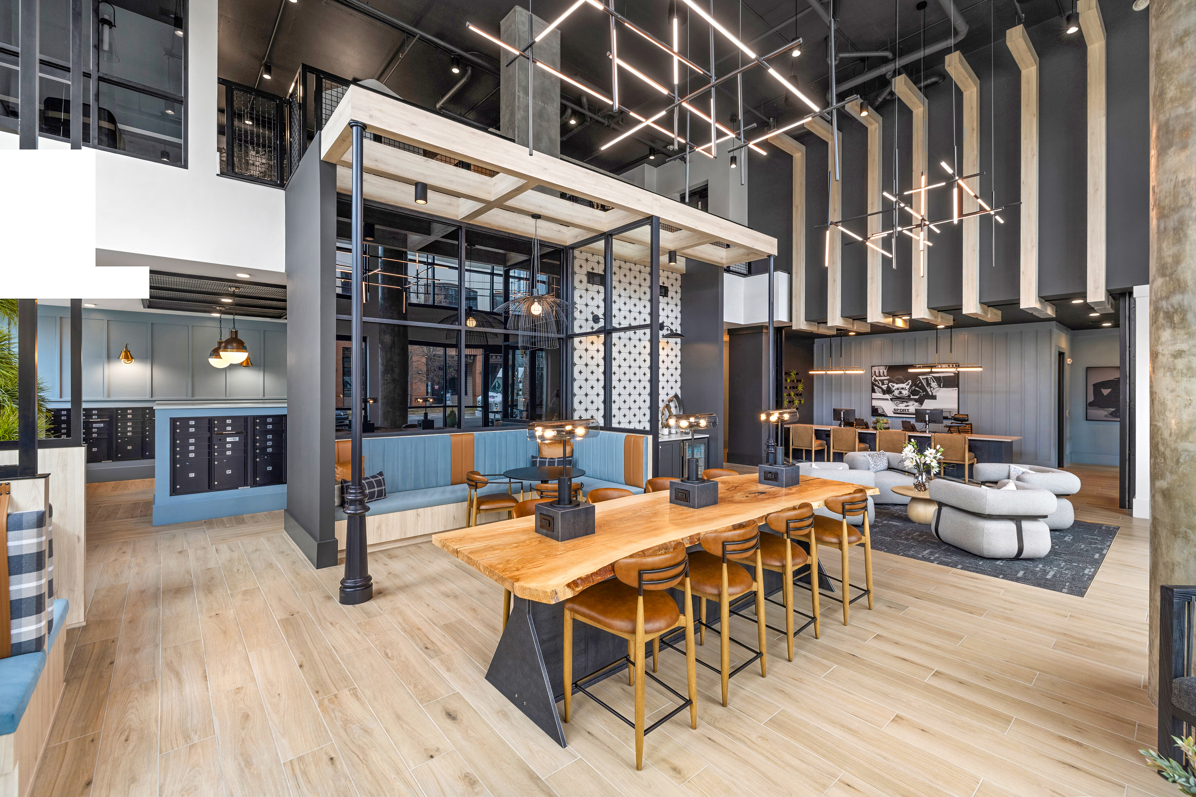 Coworking lounge long wood table with chairs next to seating areas with stylish hanging light fixtures on wood floors at MAA Plaza Midwood luxury apartments in Charlotte, NC