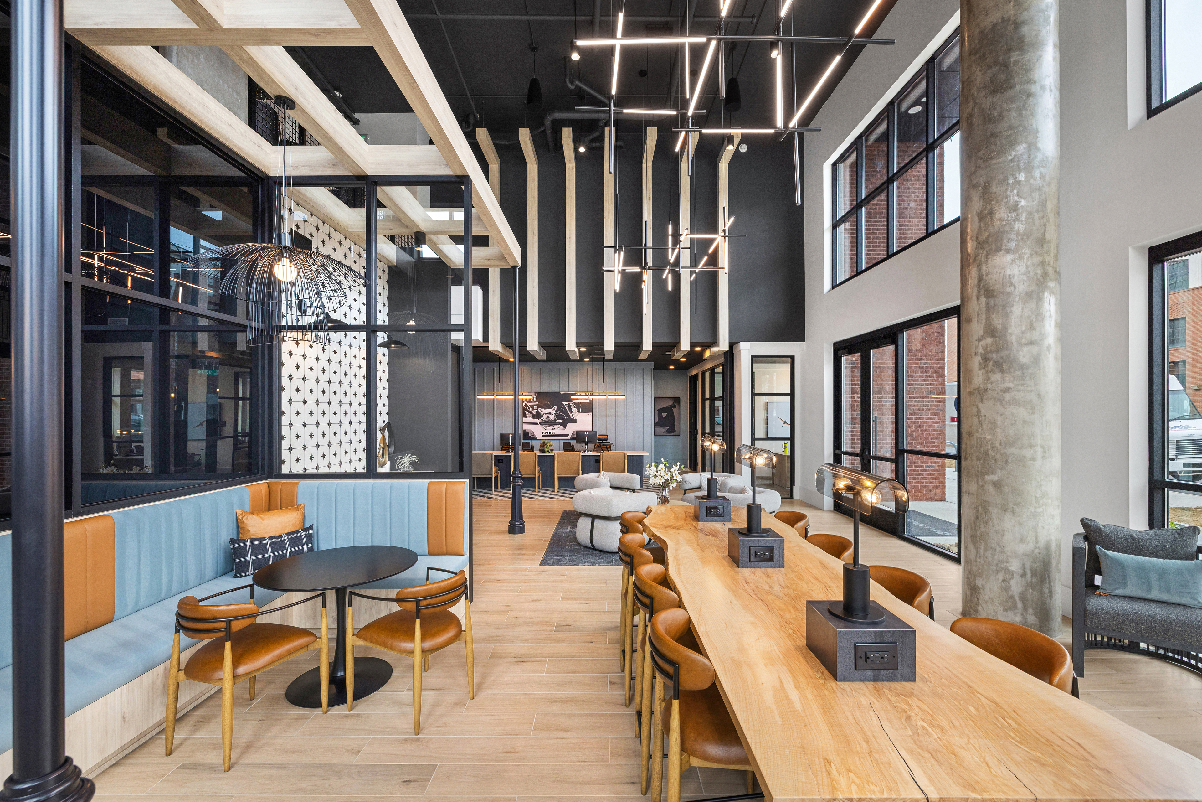 Side view of coworking lounge long wooden table next to booth seating area on wood floors at MAA Plaza Midwood luxury apartments in Charlotte, NC