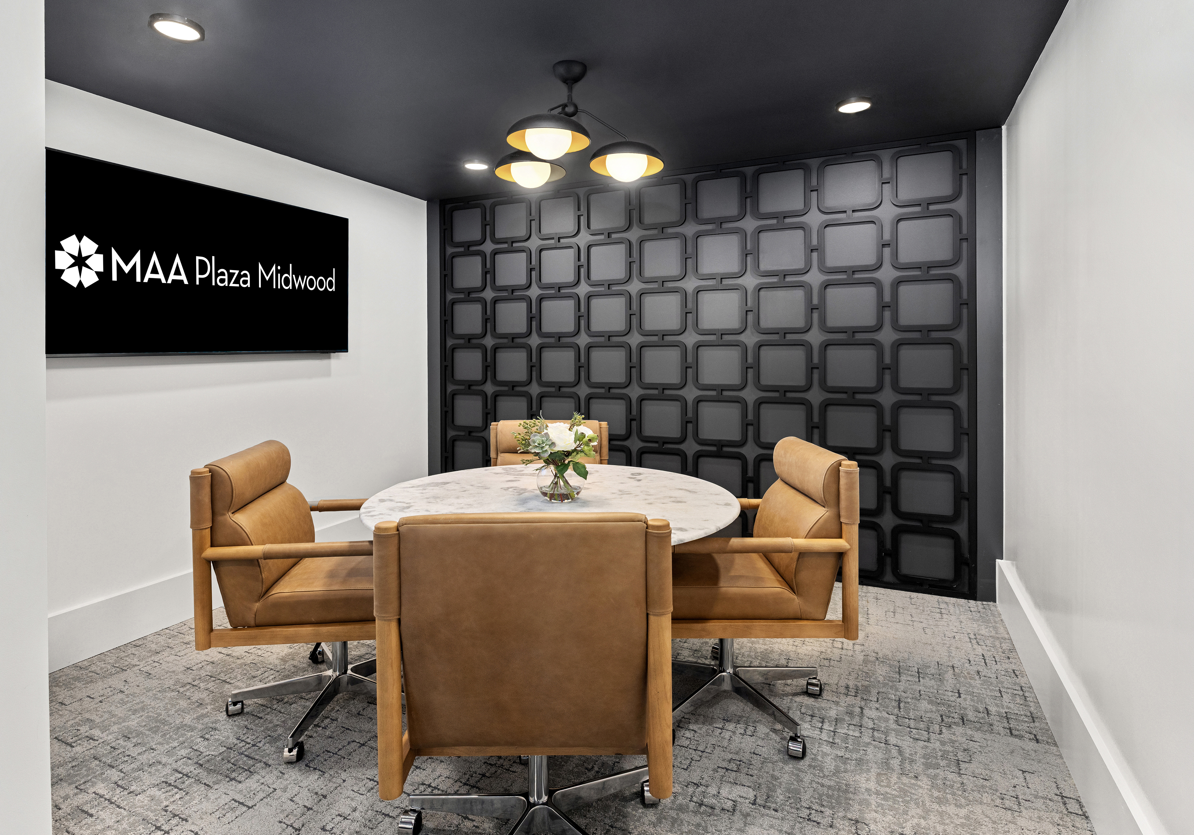Community conference room with round table and cushioned chairs with a sound board wall and signage at MAA Plaza Midwood luxury apartments in Charlotte, NC