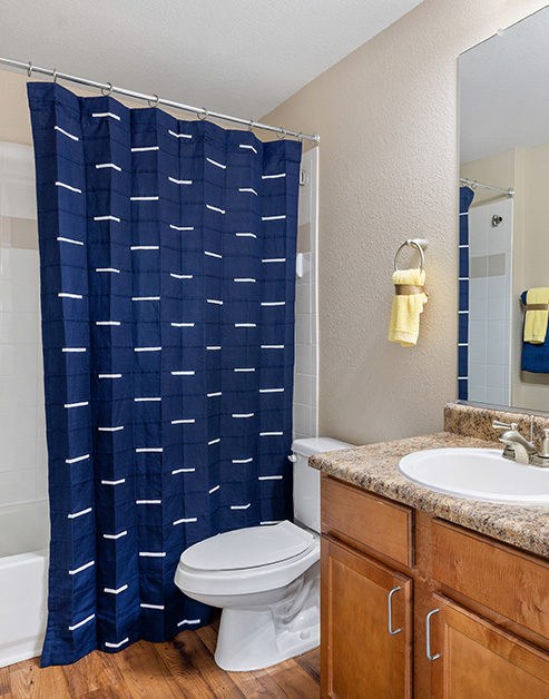 Bathroom with a vanity mirror, granite countertop with sink and brown cabinets, and dark wood floors at MAA Prosperity Creek luxury apartments in Charlotte, NC