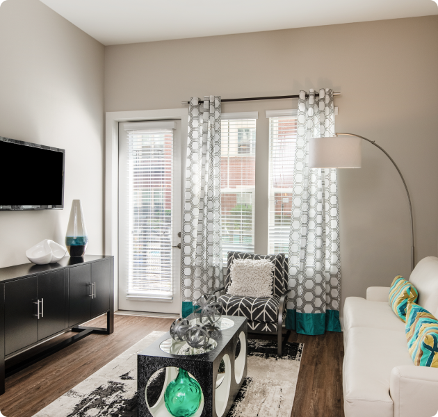 Apartment living room with white couch with coffee table and chair, wall mounted TV and dark wood cabinet next to a French door with wood floors at MAA Reserve luxury apartments in Charlotte, NC