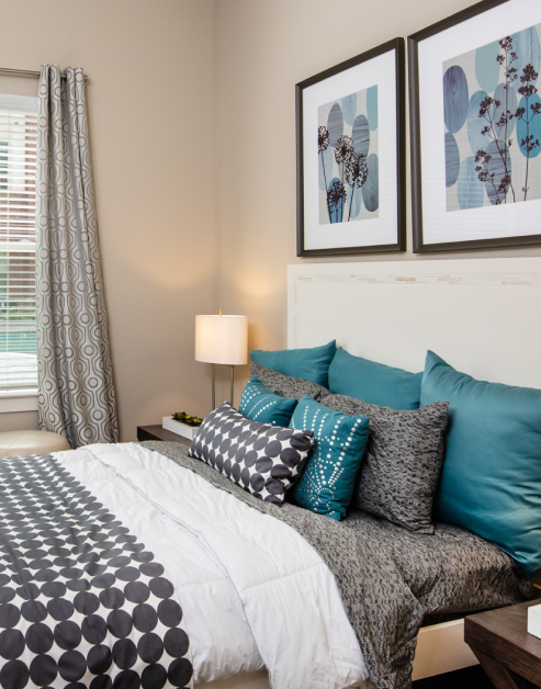 Model bedroom with wall art above queen bed and nightstand next to window with blinds at MAA Reserve luxury apartments in Charlotte, NC