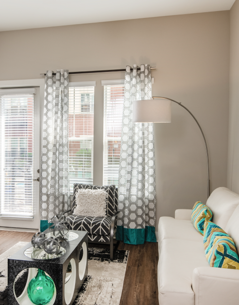 Model living room with white couch, chair and coffee table on area rug with wood floors next to windows with blinds and a French door in natural light at MAA Reserve luxury apartments in Charlotte, NC