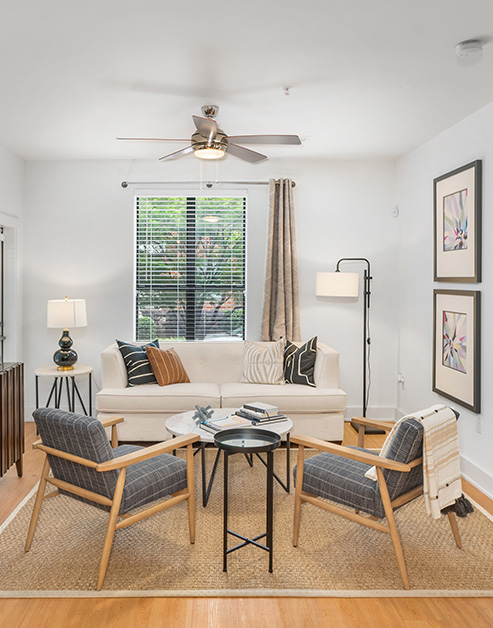 Model living room sitting area with a round coffee table and white couch next to window with blinds and curtains on wood floors at MAA South Line luxury apartments in Charlotte, NC