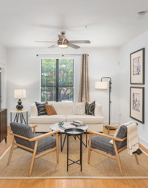 Model living room sitting area with a round coffee table and white couch next to window with blinds and curtains on wood floors at MAA South Line luxury apartments in Charlotte, NC