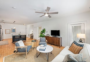 Living room with a ceiling fan, a TV on a wooden cabinet next to wood armchairs and a couch with coffee table and area rug at MAA South Line luxury apartments in Charlotte, NC