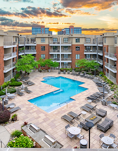 Aerial sunset view of resort-style pool with entry steps, lounge chairs surrounded by lush greenery next to the apartment complex at MAA South Line luxury apartments in Charlotte, NC