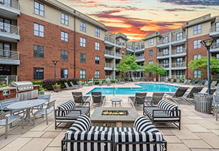Long view of poolside area with multiple sitting areas with striped cushions, next to fire pit and outside grill station at MAA South Line luxury apartments in Charlotte, NC
