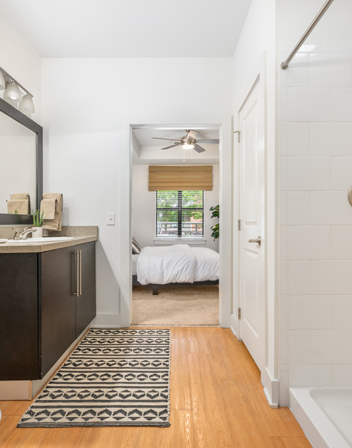En suite bathroom doorway view with wood floors and a framed vanity mirror, countertop with sink and dark cabinets at MAA South Line luxury apartments in Charlotte, NC