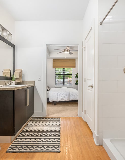En suite bathroom doorway view with wood floors and a framed vanity mirror, countertop with sink and dark cabinets at MAA South Line luxury apartments in Charlotte, NC
