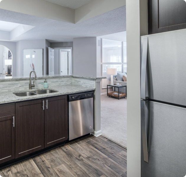 Apartment kitchen with stainless steel fridge, double sink and bar top counter with dark brown cabinets next to the living area at MAA South Park luxury apartments in Charlotte, NC
