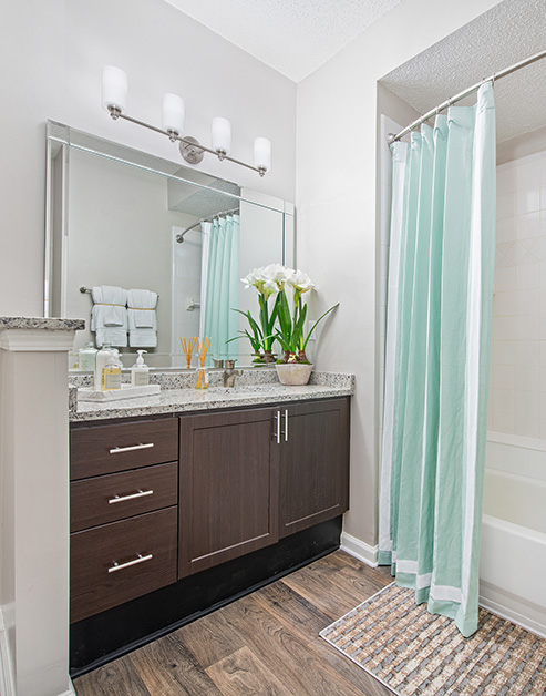 Modern bathroom with large vanity mirror, granite counter top and dark brown cabinets with wood floors at MAA South Park luxury apartments in Charlotte, NC