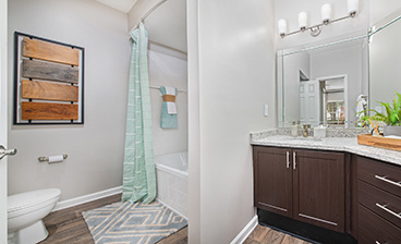 Bathroom with shower and bathtub, vanity mirror above granite counter top with dark brown cabinet and wood floors at MAA South Park luxury apartments in Charlotte, NC