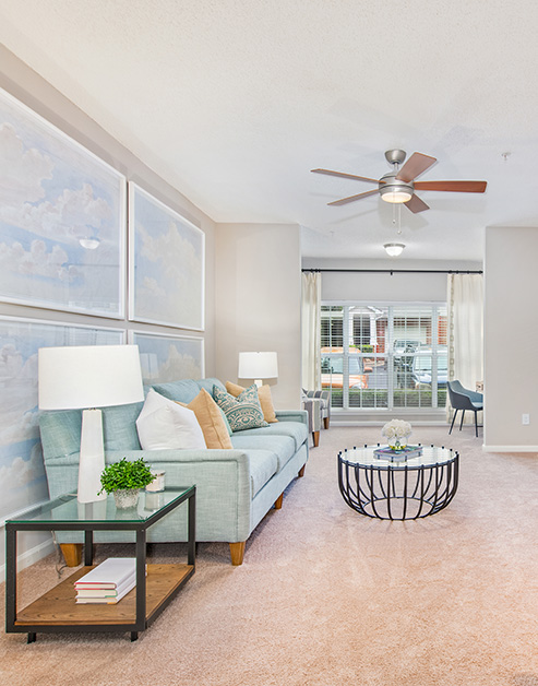Spacious living room with ceiling fan and large wall paintings with multiple sitting areas and large picture window with curtains at MAA South Park luxury apartments in Charlotte, NC