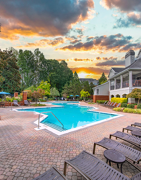 Resort-style swimming pool with entrance steps and handrails, surrounded by lounge chairs and lush greenery at MAA South Park luxury apartments in Charlotte, NC
