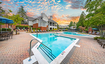Side view of resort-style swimming pool with entrance steps on brick with lounge chairs, patio tables and chairs at MAA South Park luxury apartments in Charlotte, NC