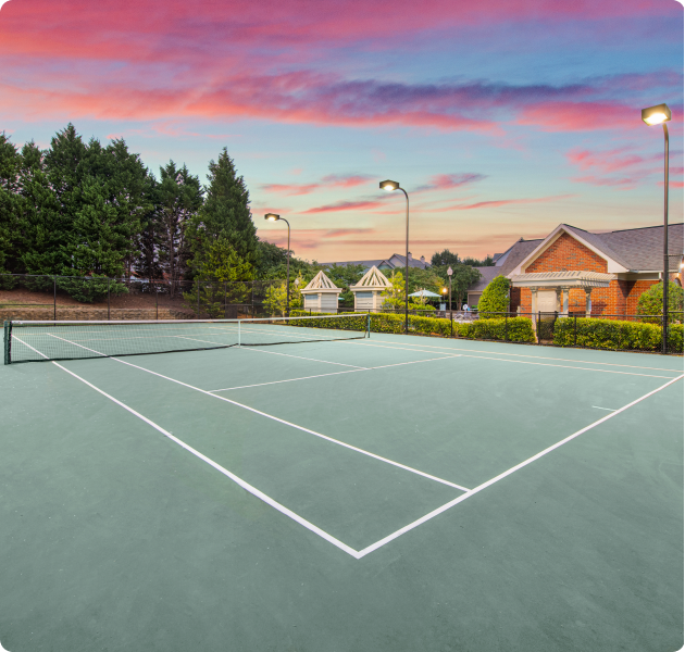 Community tennis court area with lights surrounded by lush greenery at sunset at MAA University Lake luxury apartments in Charlotte, NC