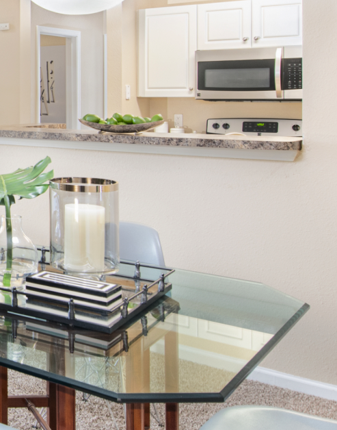 Kitchen with white cabinets, upgraded appliances bar top counter next to dining area with a glass table at MAA University Lake luxury apartments in Charlotte, NC