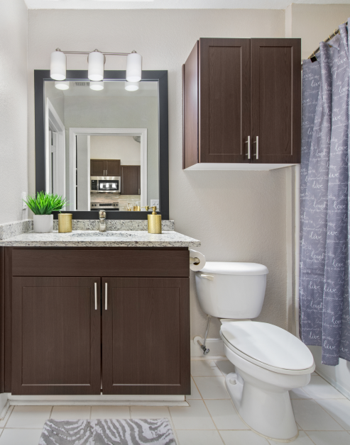 Bathroom with dark brown cabinets and a framed vanity mirror with light fixtures next to overhead cabinets above toilet at MAA Uptown luxury apartments in Charlotte, NC