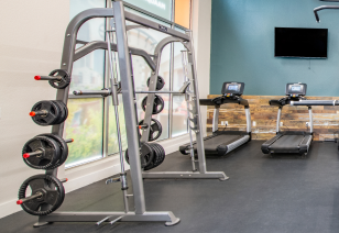 Fitness center with free weights rack and treadmills next to large window views at MAA Uptown luxury apartments in Charlotte, NC
