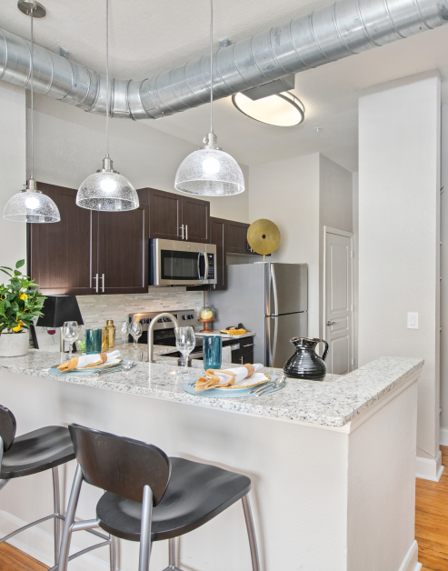 Kitchen with hanging light fixtures, dark brown cabinets, stainless steel appliances and bar top counter with chairs at MAA Uptown luxury apartments in Charlotte, NC