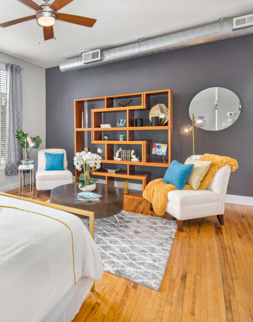 Studio living room with ceiling fan, wooden bookshelf, coffee table and chairs with an area rug next to a bed on wood floors at MAA Uptown luxury apartments in Charlotte, NC