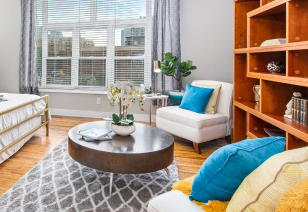 Side view of model living room with large picture window next to a bed, coffee table and white cushion chairs with pillows at MAA Uptown luxury apartments in Charlotte, NC