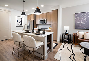 Upscale kitchen with kitchen island, stainless steel appliances, wood cabinets and tiled backsplash on wood floors next to living area at MAA Nixie luxury apartments in Durham, NC