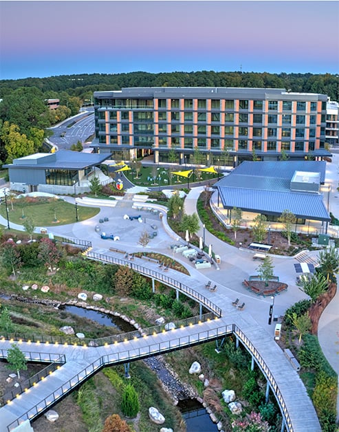 An aerial view at sunset of an apartment complex with clubhouse, park-like settings featuring walkways, bridges, and recreational areas at MAA Nixie luxury apartments in Durham, NC