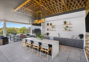 Top floor enclosed terrace lounge with a large bar top table and chairs with a communal kitchen counter with sink under an ornate ceiling panel with a hanging light fixture, and multiple sitting areas with an skyline view at MAA Nixie luxury apartments in Durham, NC