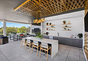 Top floor enclosed terrace lounge with a large bar top table and chairs with a communal kitchen counter with sink under an ornate ceiling panel with a hanging light fixture, and multiple sitting areas with an skyline view at MAA Nixie luxury apartments in Durham, NC