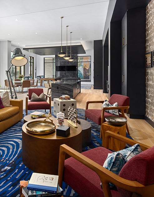 Modern clubhouse with multiple stylish lounge sitting areas, wall-mounted TV next to a communal kitchen bar with hanging light fixtures, and floor length picture windows at MAA Nixie luxury apartments in Durham, NC