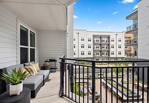 Second-story outdoor patio with lounge sofas and metal railing with a view overlooking courtyard at MAA Nixie luxury apartments in Durham, NC
