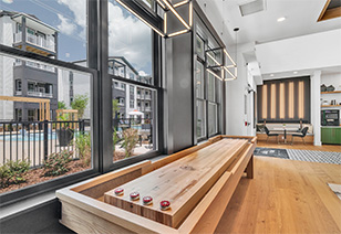 Clubhouse with shuffleboard table next to large picture windows on wood floors at MAA Vale luxury apartments in Raleigh, NC