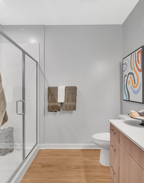 Modern bathroom with glass shower doors with grey walls and towel rack on light wood floors at MAA Vale luxury apartments in Raleigh, NC