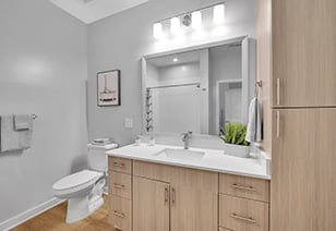 Modern bathroom with sleek light fixtures above a framed vanity mirror with white countertops and sink with light brown cabinets at MAA Vale luxury apartments in Raleigh, NC