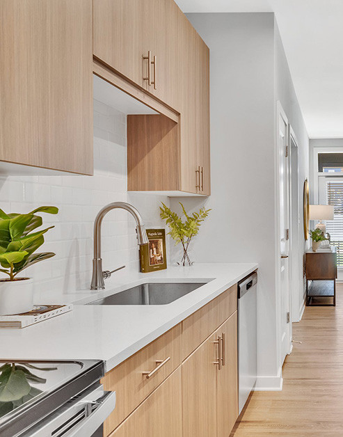 Modern kitchen with light-colored wood cabinets and white counters with sink and stainless steel appliances on wood floors at MAA Vale luxury apartments in Raleigh, NC