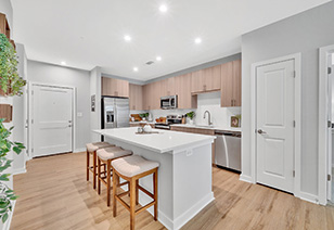 Open-style kitchen with light-colored wood cabinets and stainless steel appliances with a white island with wood barstools on wood floors at MAA Vale luxury apartments in Raleigh, NC