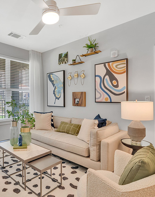 Modern living room with wall art above an off-white couch and armchair next a small rectangular coffee table on an area rug at MAA Vale luxury apartments in Raleigh, NC