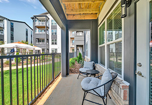 Living room balcony with dark grey metal railings and light grey upholstered chairs with a grassy view at MAA Vale luxury apartments in Raleigh, NC